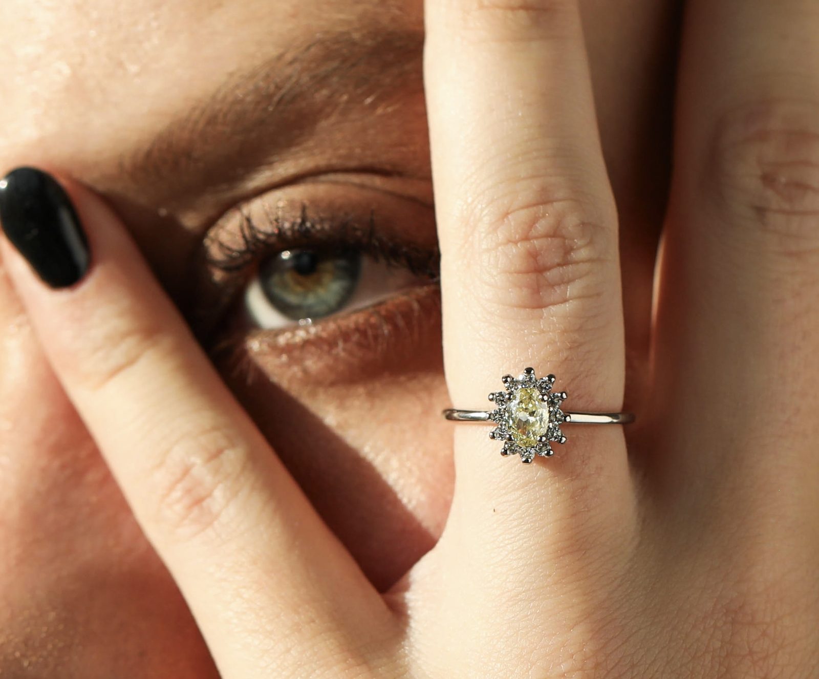 Anillo solitario de diamante amarillo en la mano de una modelo, junto al rostro