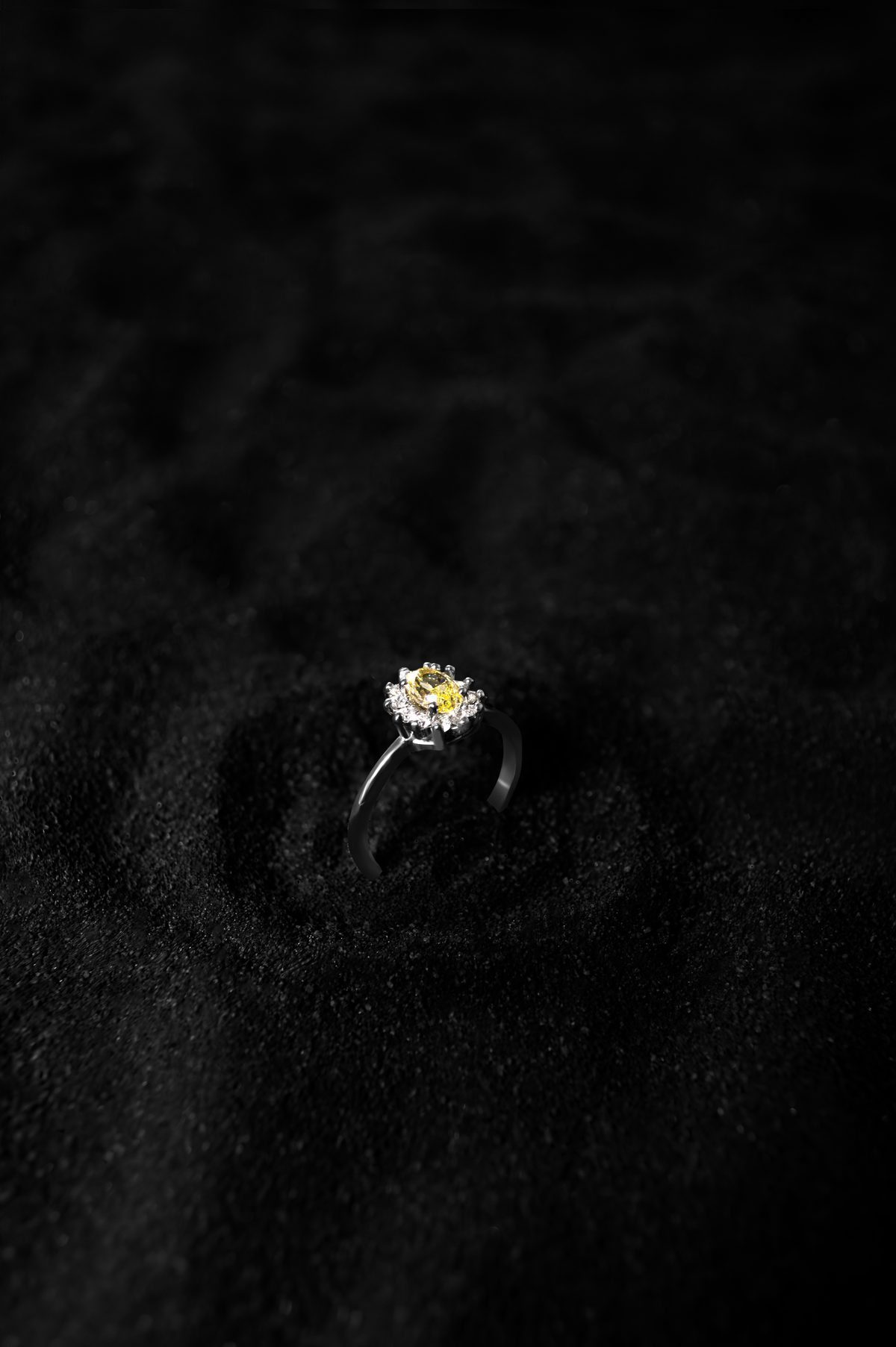 Anillo YS.05 con diamante amarillo oval y halo floral de diamantes blancos en oro blanco 18k, sobre arena negra